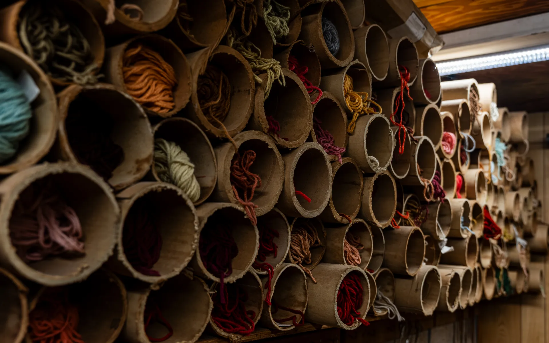Wall of cardboard tubes filled with yarn sorted by color, from teal and rust to burgundy and cream