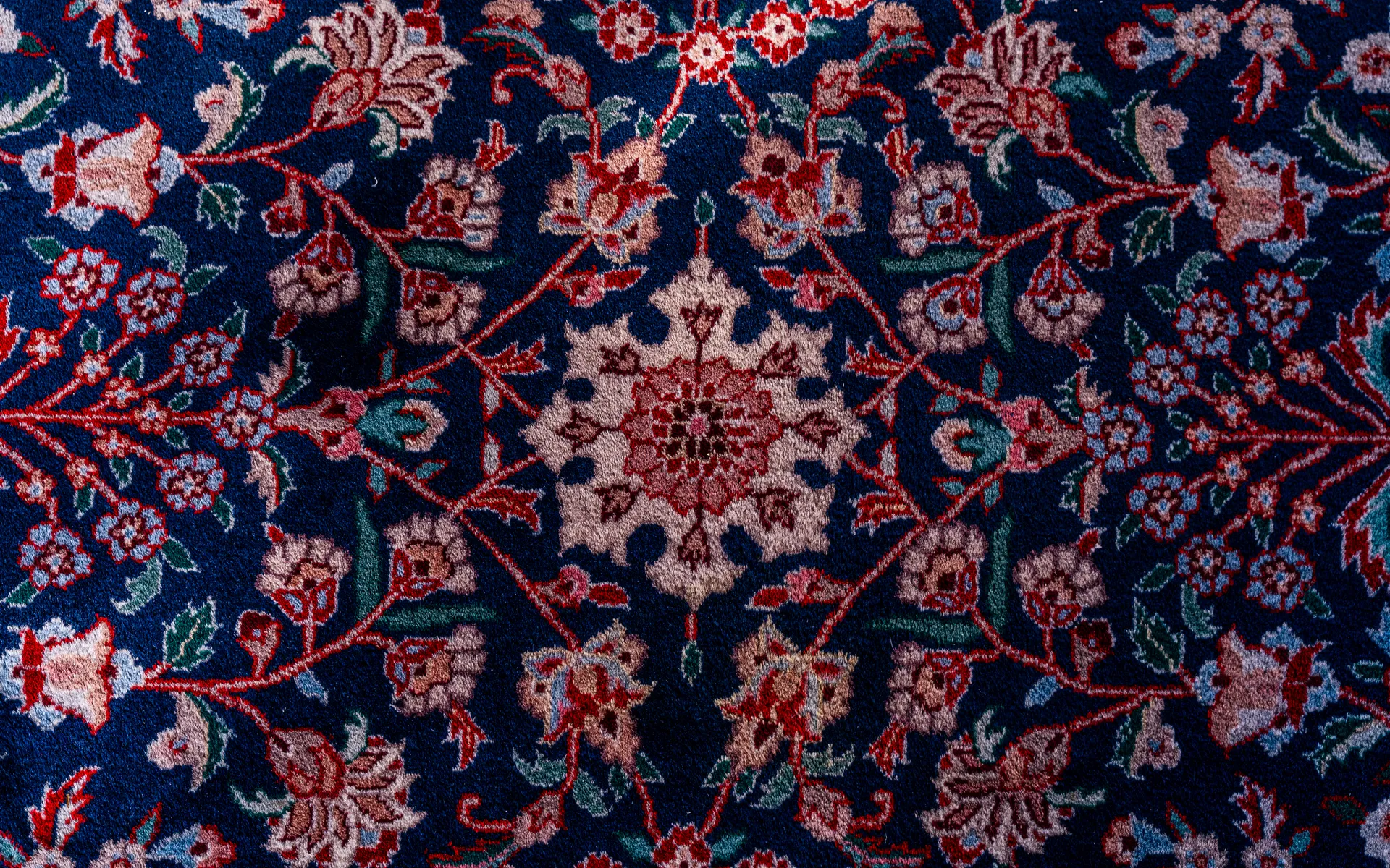 Top-down close-up of a navy oriental rug's pile with an ivory center rosette, red vines and pink, blue and teal flowers