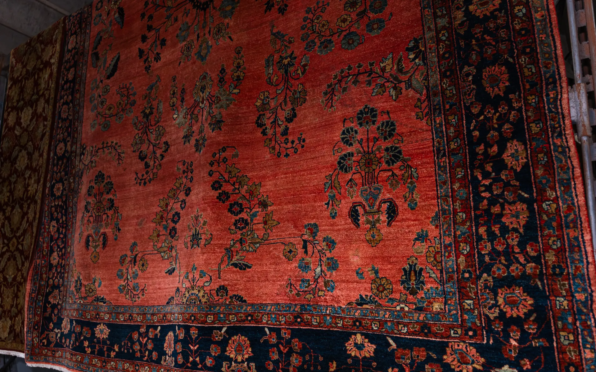 Close-up of a red Persian-style rug with scattered floral sprays and a deep navy floral border on display in a shop